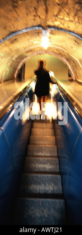 Woman riding escalator at night, rear view Stock Photo