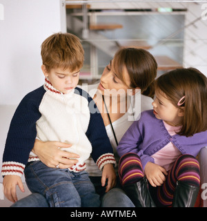 Mother sitting with children, looking at son Stock Photo