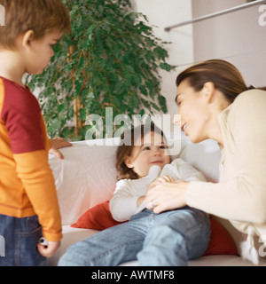 Woman holding daughter on couch, son standing nearby Stock Photo