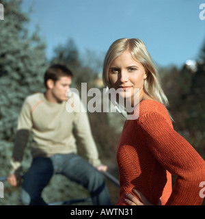 Woman standing, hands on hips, man sitting on railing in background Stock Photo