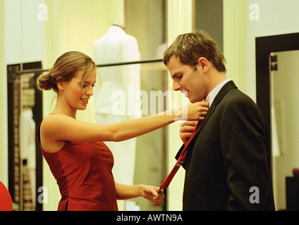 Woman holding neck tie up to man's neck in clothing store, side view. Stock Photo