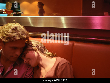 Couple sitting in booth, woman leaning head on man's shoulder Stock Photo