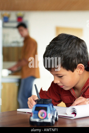 Son writing, father in background blurred. Stock Photo