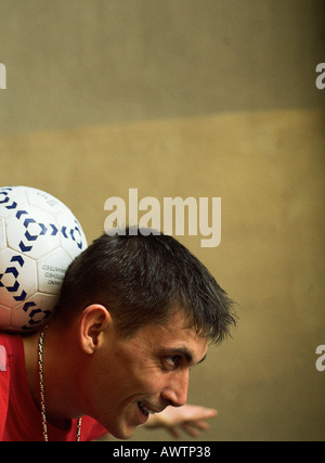 Profile of man balancing soccer ball on back of neck Stock Photo