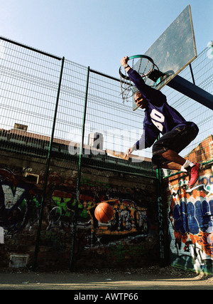 Man hanging on basketball rim after dunking ball Stock Photo