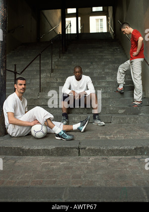 Three men sitting on steps with soccer ball Stock Photo