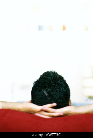 Man sitting with hands behind head, rear view Stock Photo
