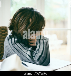 Child leaning on table, looking out window, distracted from doing homework Stock Photo