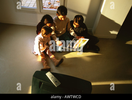 Young boys and girls sitting on floor looking at a book, high angle view Stock Photo