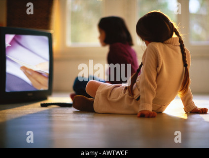 Young girls sitting on wood floor watching TV, girl in background blurred Stock Photo