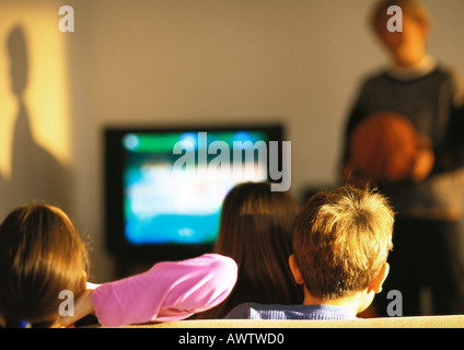 Young boys and girls watching TV, boy in distance blurred Stock Photo