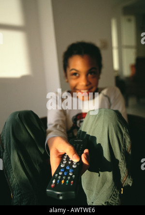 Young girl sitting, pointing remote control, smiling Stock Photo