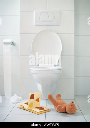 Open book and teddy bear on floor in front of toilet Stock Photo