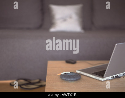 Laptop on table next to ashtray, sofa in background Stock Photo