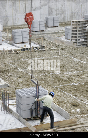 Worker guiding crane lifted palette of breeze blocks on building site Stock Photo