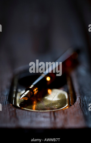 Old wooden school desk with a ink well and fountain pen lit by candlelight. Cumbria, UK Stock Photo