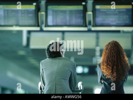 Businessman and businesswoman sitting under airport departure and arrival monitors, rear view Stock Photo