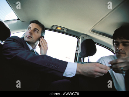 Businessman on cell phone in backseat of car paying taxi driver, low angle view Stock Photo