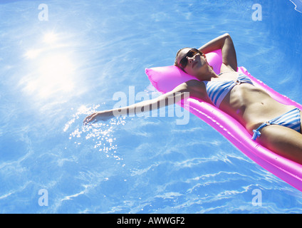 Woman sunbathing on air mattress in pool Stock Photo