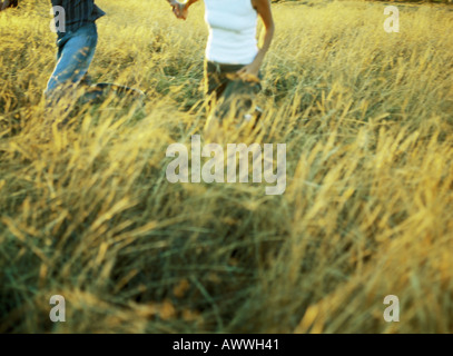 Couple running in field of tall grass, mid-section Stock Photo