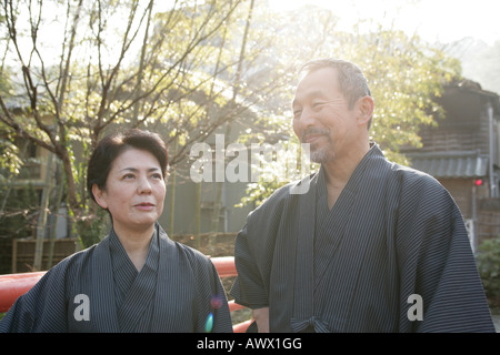 Elderly couple standing on bridge in garden, smiling Stock Photo