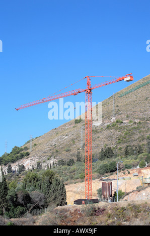 Single crane and new construction site on side of mountain in sunny Spain Stock Photo