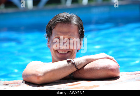 Smiling man lying on side of swimming pool in the sun on vacation Stock Photo