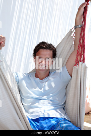 Handsome middle aged man sitting in hammock and smiling at the camera on a sunny day Stock Photo