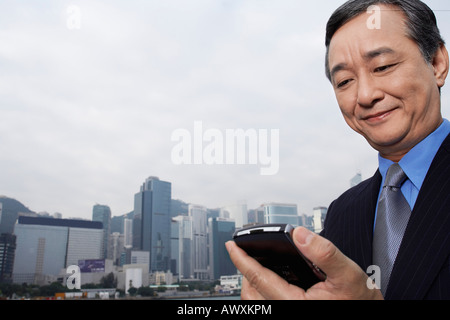 Middle-aged business man using PDA, office buildings in background Stock Photo