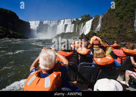Tourist on the iver boat ride getting up close to the falls Iguassu Falls is the largest series of waterfalls on the planet Stock Photo