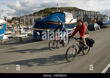 Young couple cycling on Aberystwyth harbour quayside Wales UK Stock Photo