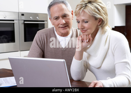 Middle-aged couple counting bills using laptop in kitchen Stock Photo