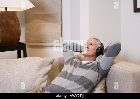 Middle-aged man listentening to music on headphones in living room Stock Photo