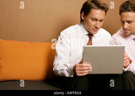 Two businessmen using laptop, sitting on sofa Stock Photo