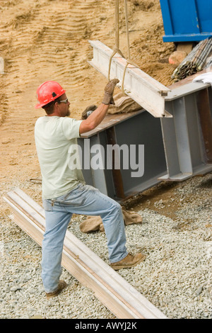 A construction worker wearing a red hard-hat, guides a steel girder into position. Stock Photo