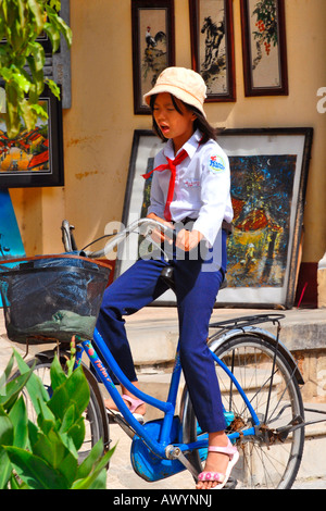 Asia Far East Vietnam Hoi An market , one pretty young girl riding on bike in traditional communist style school uniform & floppy sun hat Stock Photo