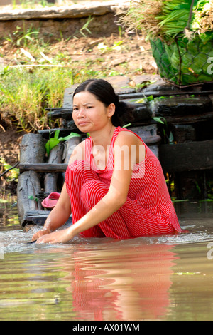 Asia Far East Vietnam , Mekong Delta , pretty young girl with long black hair in national dress washes clothes in river while sitting in water Stock Photo
