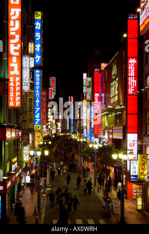 Busy scene at night with many bright glowing signs and people walking in street in Shinjuku Tokyo Japan Stock Photo