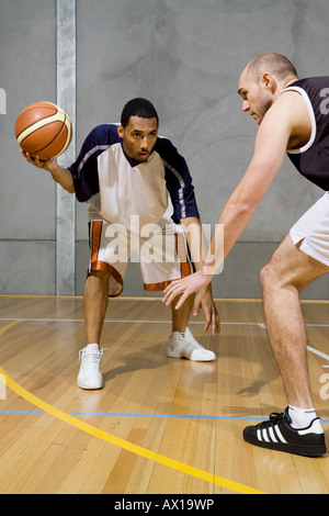 One basketball player dribbles the ball and another player guards him Stock Photo