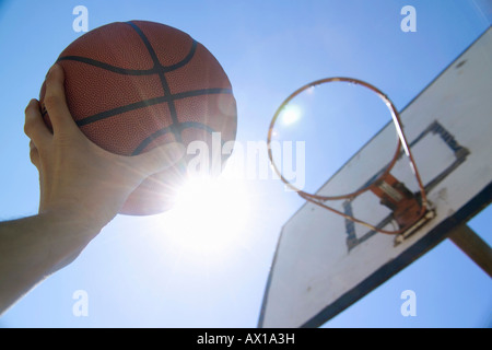 A human hand reaching up towards the sun and basketball hoop with holding basketball Stock Photo