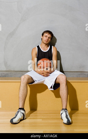 A young man sitting on a bench on a basketball court Stock Photo