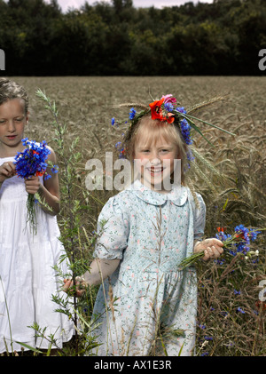 Two girls in a wheat field with bunches on wildflowers Stock Photo
