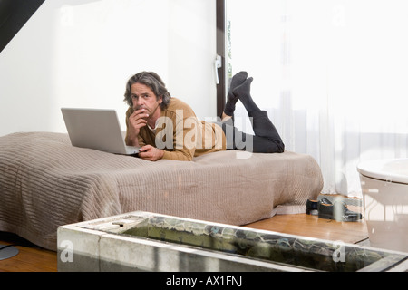 A man lying on a bed and using a laptop Stock Photo