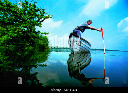 Man in small boat measuring water levels in brim full reservoir at Bewl Water in Kent. He is a Southern Water Company employee Stock Photo