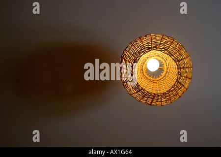 Ceiling with an illuminated light bulb and pendant shade in a bedroom Stock Photo