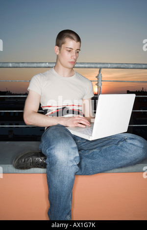 A young adult man using a laptop computer on a rooftop terrace Stock Photo