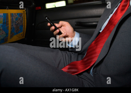 Midsection of a businessman sitting in a taxi and using a mobile phone Stock Photo