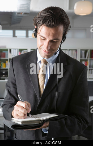 A man wearing a telephone headset and writing in a personal organizer Stock Photo