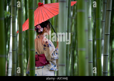 A woman wearing a kimono and standing in a bamboo grove