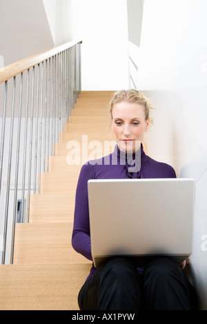 A mid adult woman sitting on a staircase using a laptop Stock Photo